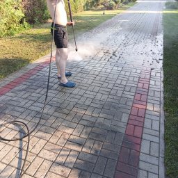Fornalpol - Mężczyzna w klapkach i czarnych spodenkach czyści kostkę brukową myjką ciśnieniową na zewnątrz, widoczny efekt czyszczenia.