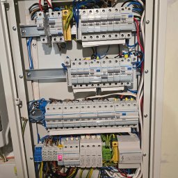 Elektromonter - Otwarta skrzynka rozdzielcza z widocznymi bezpiecznikami, przewodami różnego koloru i elementami montażowymi na szynach DIN.