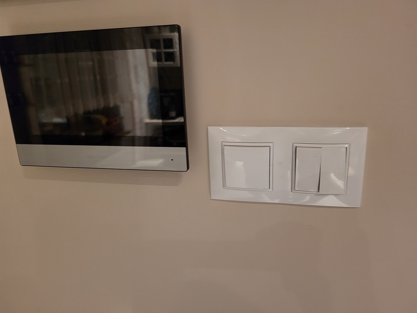 Nowoczesny wideofon z czarną obudową zamontowany na ścianie obok białego podwójnego włącznika światła.