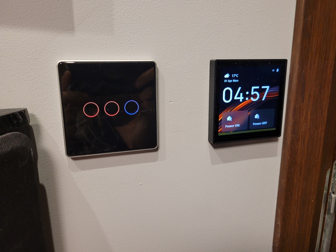 Dwa nowoczesne panele sterowania na ścianie: dotykowy włącznik z trzema podświetlanymi okręgami (dwa czerwone, jeden niebieski) oraz panel z wyświetlaczem LCD pokazującym godzinę i przyciski...