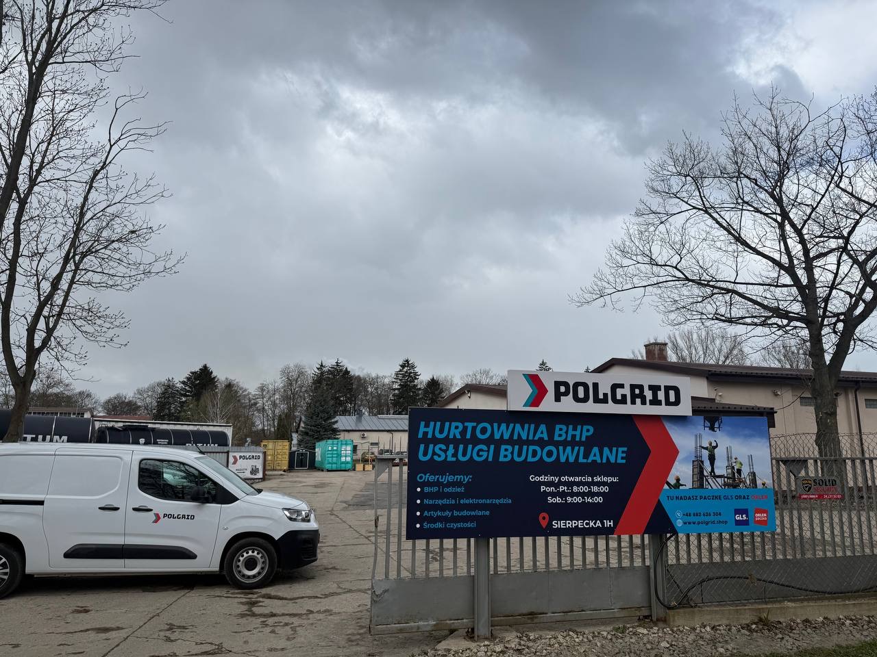 Zdjęcie przedstawia siedzibę hurtowni BHP i usług budowlanych Polgrid, z widocznym banerem reklamowym, białym samochodem dostawczym z logo firmy oraz budynkiem w tle.