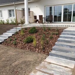 Karolina Dmitruk - Nowoczesny ogród przy białym domu z tarasem, z betonowymi schodami prowadzącymi do rabaty wysypanej korą i obsadzonej młodymi krzewami i trawami ozdobnymi.