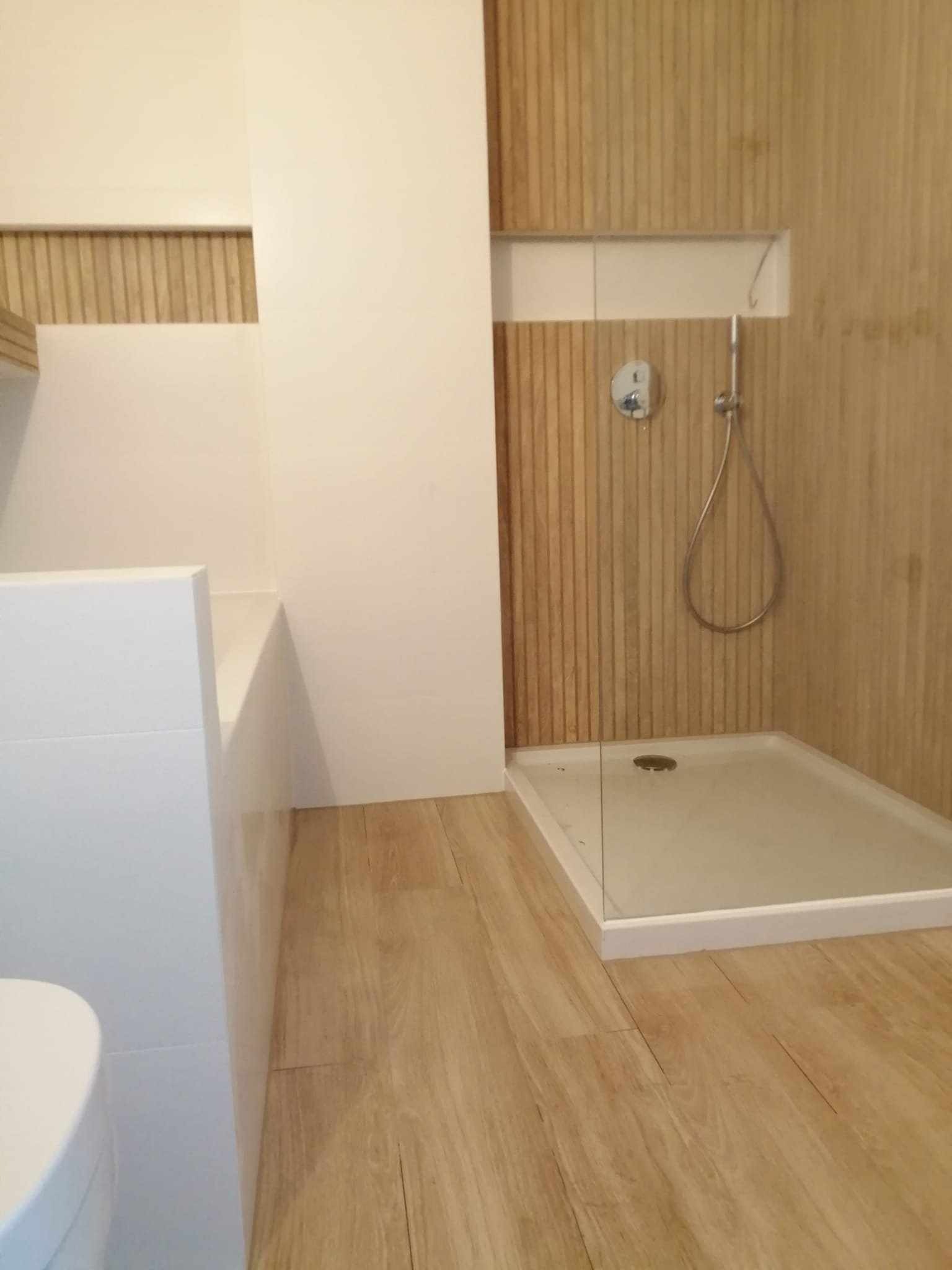 Nowoczesna łazienka z kabiną prysznicową wykończoną drewnopodobnymi panelami ściennymi, białą armaturą i podłogą z jasnego drewna.