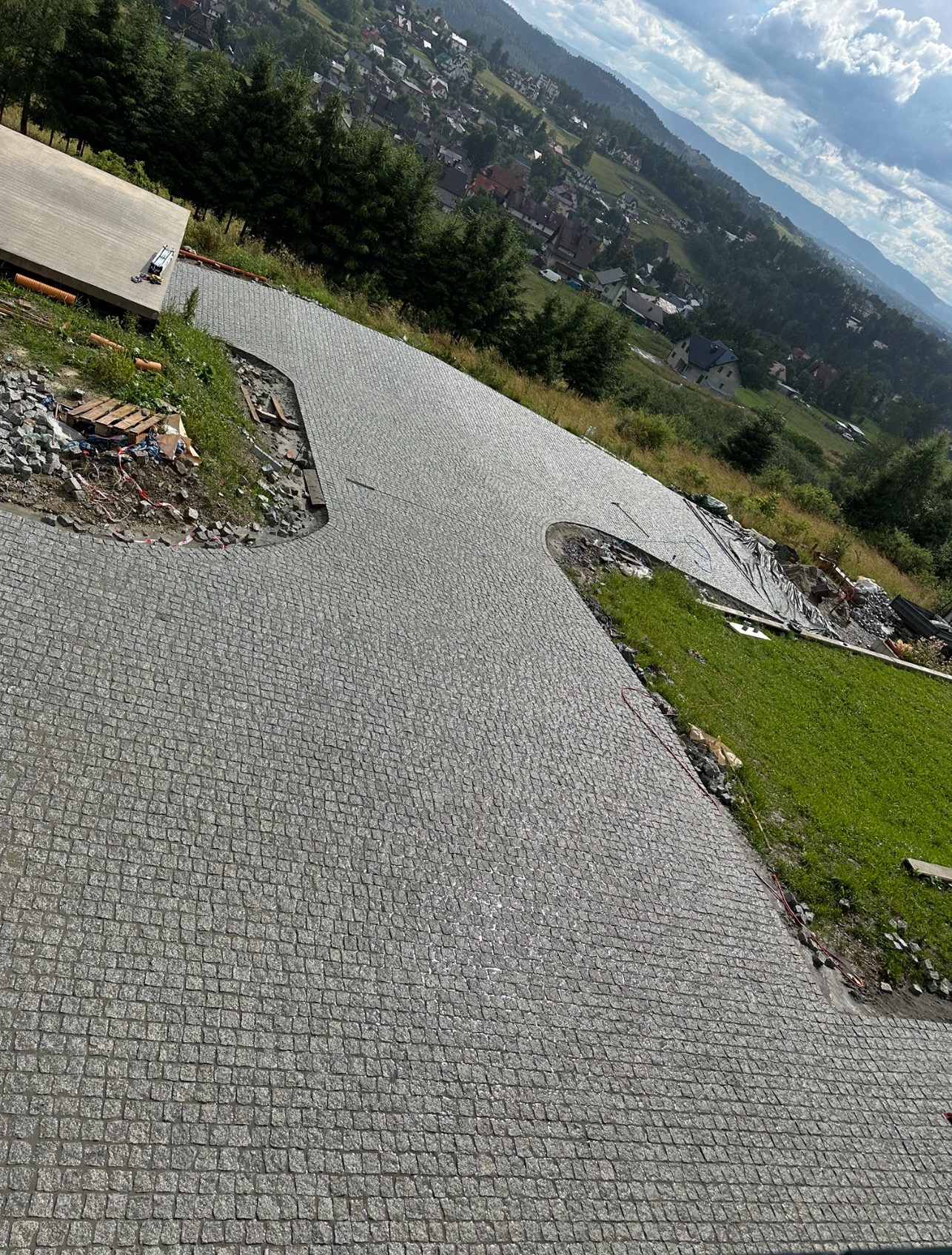 Nowo ułożona, szara kostka na podjeździe w Rudawie, z widokiem na górzysty krajobraz w tle. Kostka ułożona w regularny wzór, z widocznymi elementami przygotowania terenu po bokach.