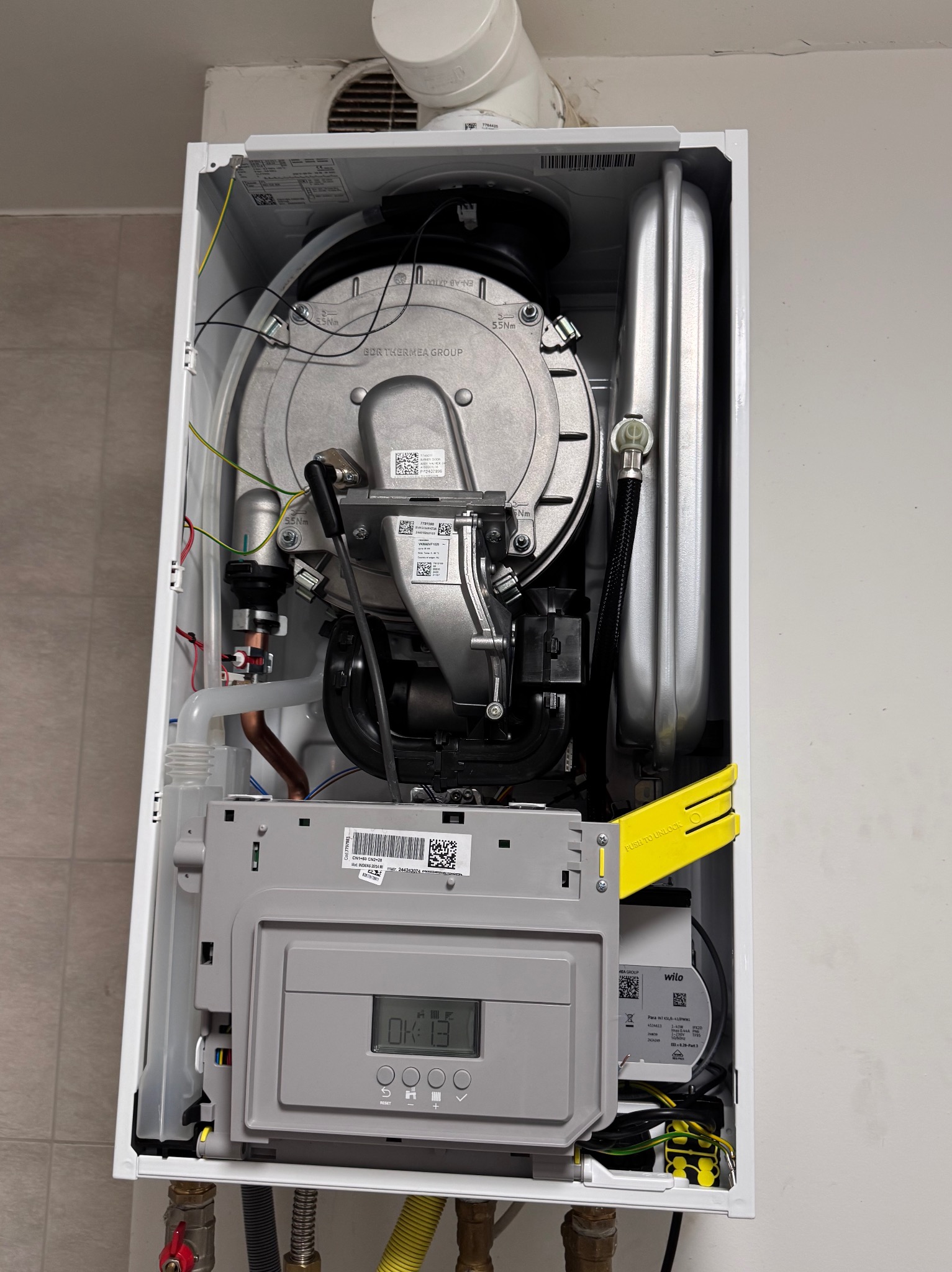 Wnętrze otwartego pieca gazowego w Godziszce. Widoczne komponenty, w tym panel sterowania z wyświetlaczem i żółty element blokujący. Precyzyjne detale instalacji.