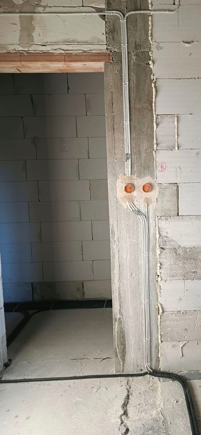 Świeżo położone, białe kable elektryczne w peszlach i rurkach na surowych ścianach z betonu komórkowego, widoczne puszki instalacyjne przed montażem osprzętu.