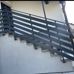 DANMAR Marcin Małyjurek - Nowoczesna, metalowa balustrada schodowa w kolorze grafitowym, zamontowana przy wejściu do budynku. Widoczne granitowe stopnie i fragment elewacji.