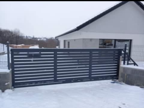 Nowoczesna, przesuwna brama wjazdowa z poziomych profili, w kolorze antracytowym, na tle zasypanego śniegiem podjazdu i minimalistycznego domu.