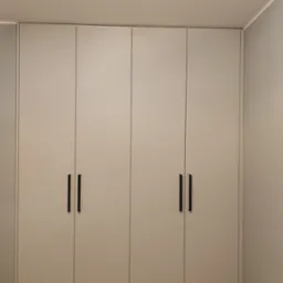 Jasnoszara szafa wnękowa z minimalistycznymi, czarnymi uchwytami, zrealizowana w Kętach. Widoczna podłoga imitująca drewno i fragment szarej ściany.