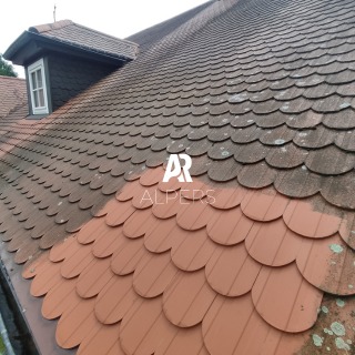 Dach pokryty dachówką karpiówką, częściowo umyty, z widoczną różnicą w kolorze i osadzie. Fragment dachu w pierwszym planie z nowszą, czystą dachówką, kontrastuje z resztą pokrycia. Widoczny...