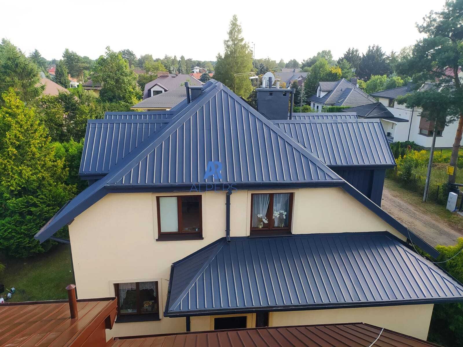 Dom jednorodzinny z nowym, grafitowym dachem z blachy na rąbek stojący; widok z góry, w tle zabudowa jednorodzinna i zieleń.