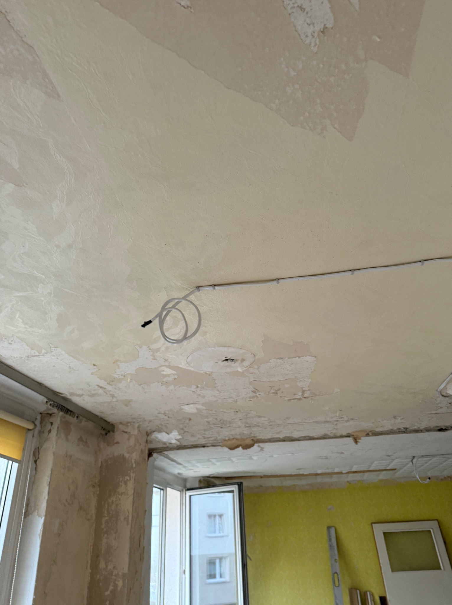 Przewód elektryczny poprowadzony po suficie w pomieszczeniu w trakcie remontu, widoczne ślady po starej farbie i tapetach.