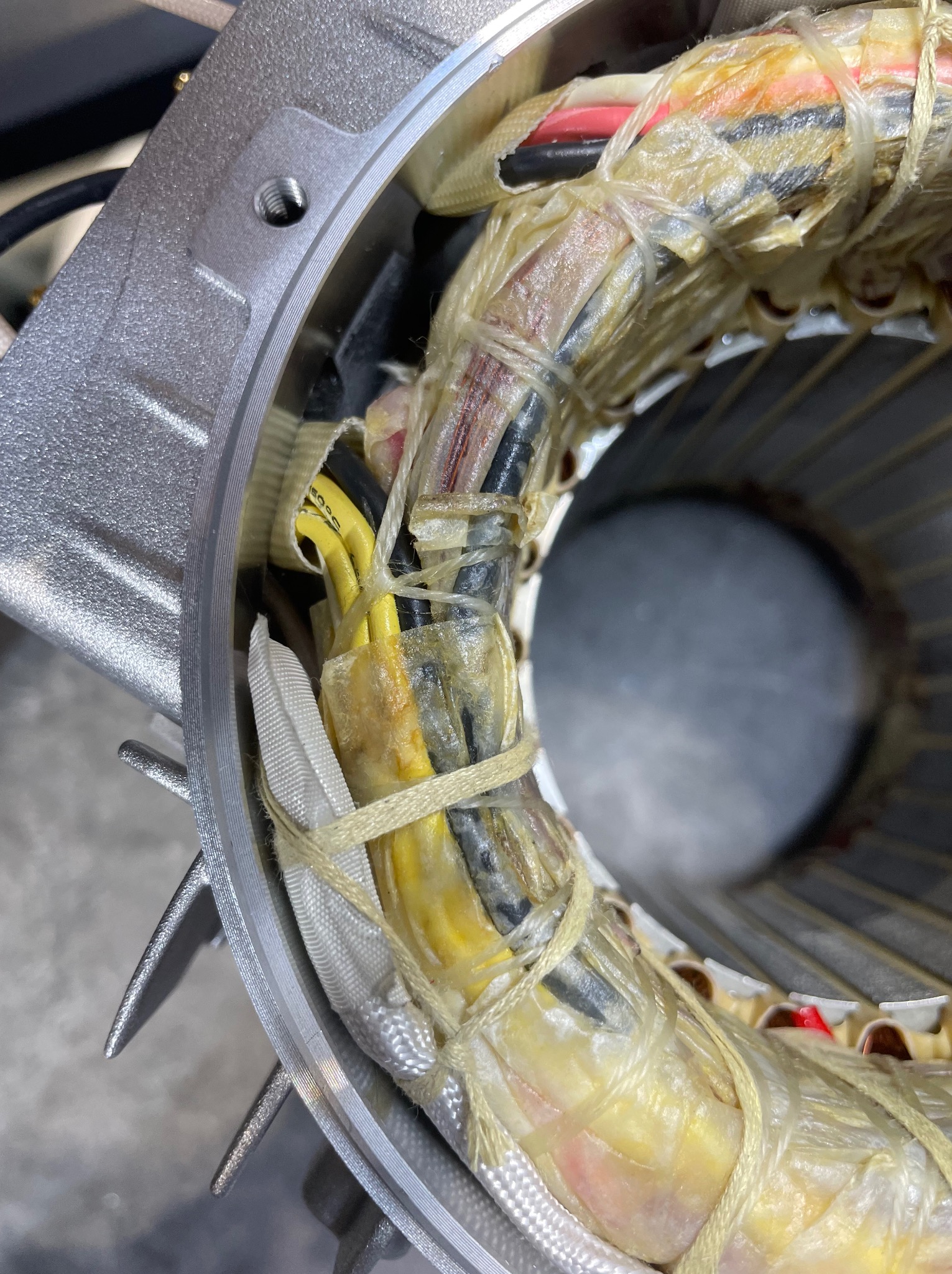 Szczegółowe zbliżenie stojana silnika elektrycznego z widocznymi uzwojeniami, izolacją i elementami mocującymi, umieszczonego w metalowej obudowie z radiatorem.