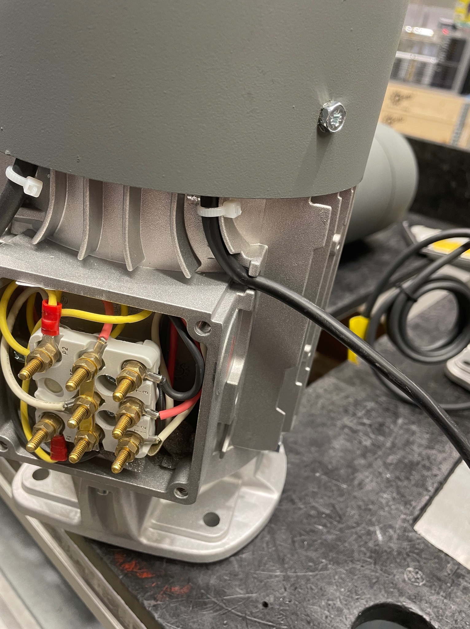 Szczegółowe ujęcie złącza elektrycznego silnika indukcyjnego z widocznymi przewodami w kolorach żółtym, czerwonym i czarnym, podłączonymi do zacisków z gwintowanymi końcówkami.