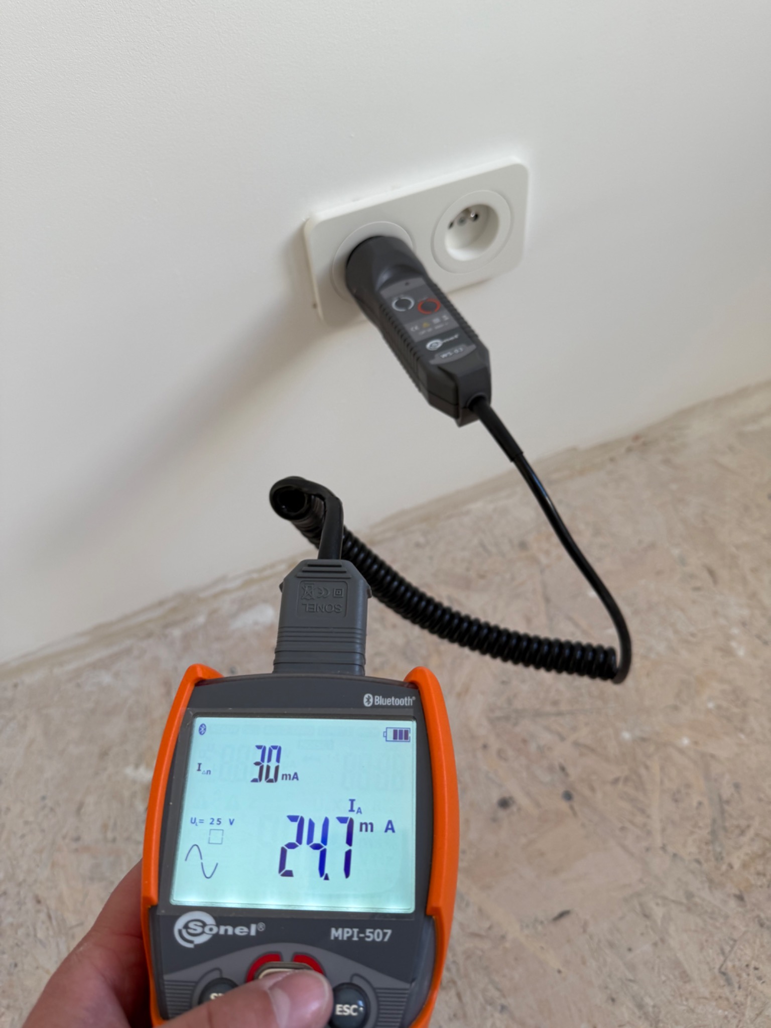 Pomiar prądu upływu w gniazdku elektrycznym za pomocą miernika Sonel MPI-507 z widocznym wskazaniem 24.7 mA na wyświetlaczu.