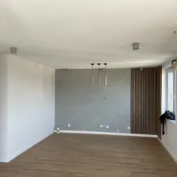 Nowoczesne wnętrze: ściana z szarej gładzi z geometrycznym wzorem, drewniana lamelowa ściana, parkiet, minimalistyczne lampy wiszące.