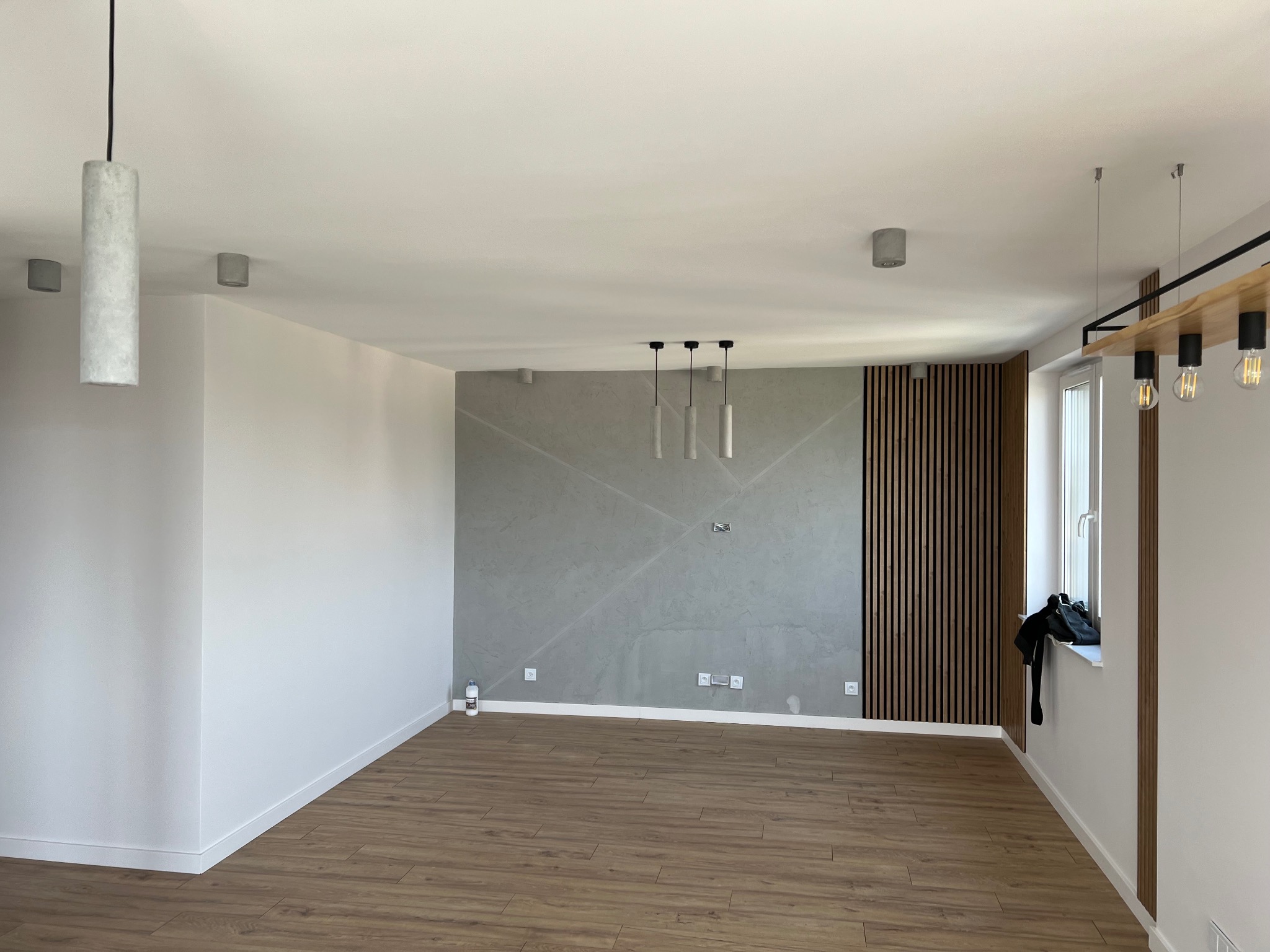 Nowoczesne wnętrze: ściana z szarej gładzi z geometrycznym wzorem, drewniana lamelowa ściana, parkiet, minimalistyczne lampy wiszące.