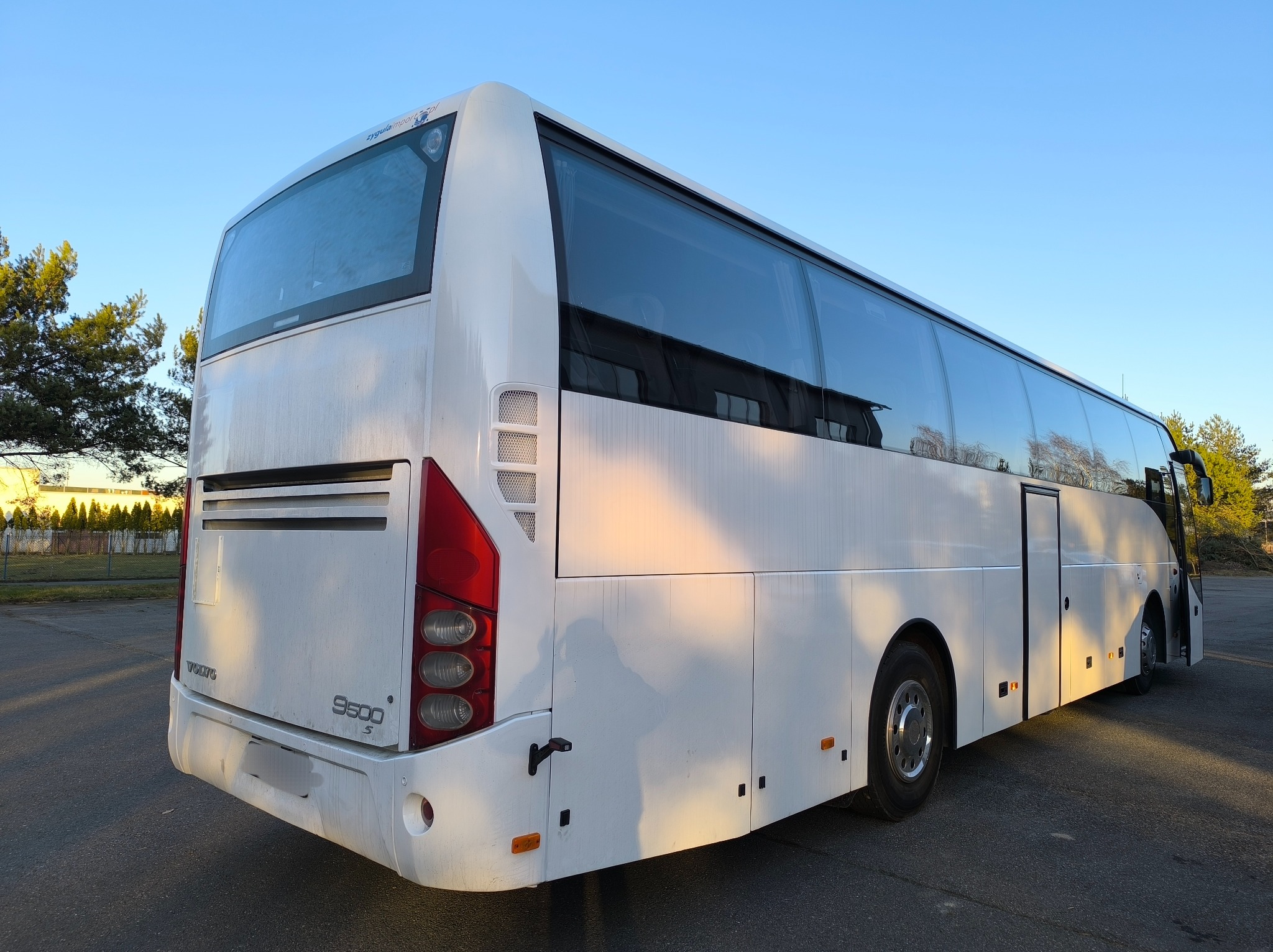 Tył białego autokaru Volvo 9500 S na parkingu, widoczne światła, szyby i logo Volvo