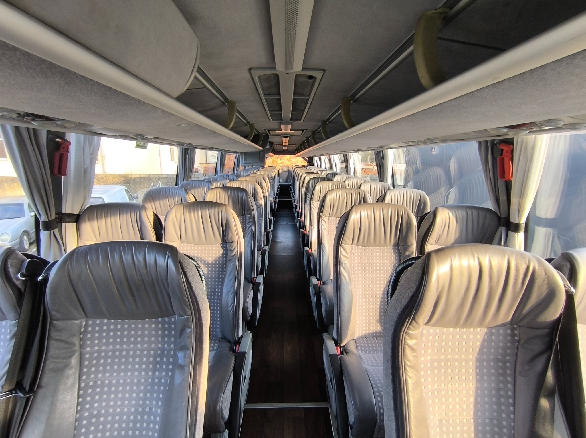 Wnętrze autobusu turystycznego z rzędami szarych skórzanych foteli z drobnym wzorem, widok z przodu kabiny na przejście.