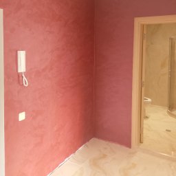 Serhii Ryzhenko - Ściana pomalowana dekoracyjną farbą w odcieniach różu, z widocznym domofonem i włącznikiem światła, oraz otwartymi drzwiami do wykończonej łazienki z kabiną prysznicową.