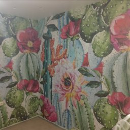 Serhii Ryzhenko - Ściana pokryta tapetą z motywem kaktusów i kwiatów w pastelowych kolorach, imitująca popękaną fakturę.