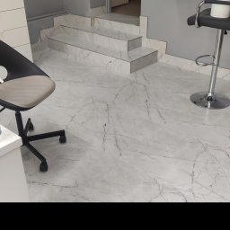 Serhii Ryzhenko - Jasnoszara marmurowa podłoga i schody w salonie kosmetycznym, widoczny fragment krzesła biurowego i stołek barowy.