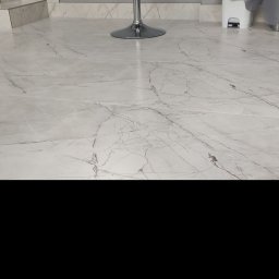 Serhii Ryzhenko - Biała podłoga z płytek imitujących marmur, widoczny fragment schodów z identycznych płytek, chromowany hoker barowy i biały kosz na śmieci w tle.