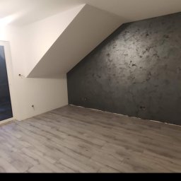 Serhii Ryzhenko - Pokój na poddaszu po remoncie: szare panele podłogowe ułożone w jodełkę, ściana pomalowana na ciemny szary kolor z efektem dekoracyjnym, białe ściany i sufit.