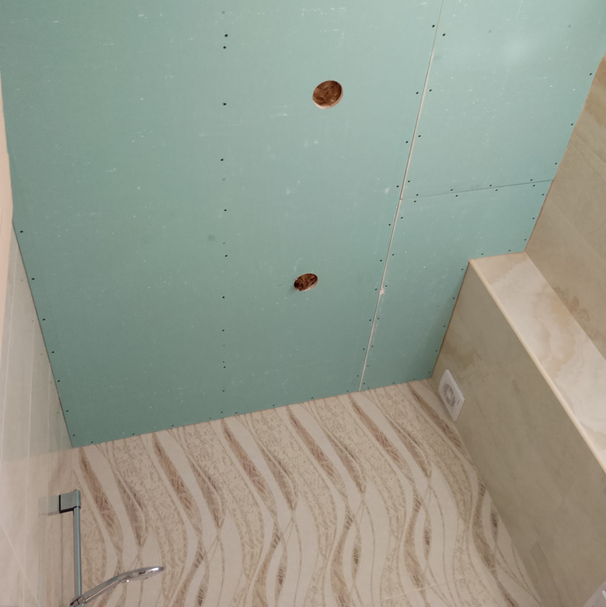 Montaż sufitu podwieszanego z płyty kartonowo-gipsowej w łazience, widoczne otwory na oświetlenie i wykończone płytki ścienne z delikatnym wzorem.