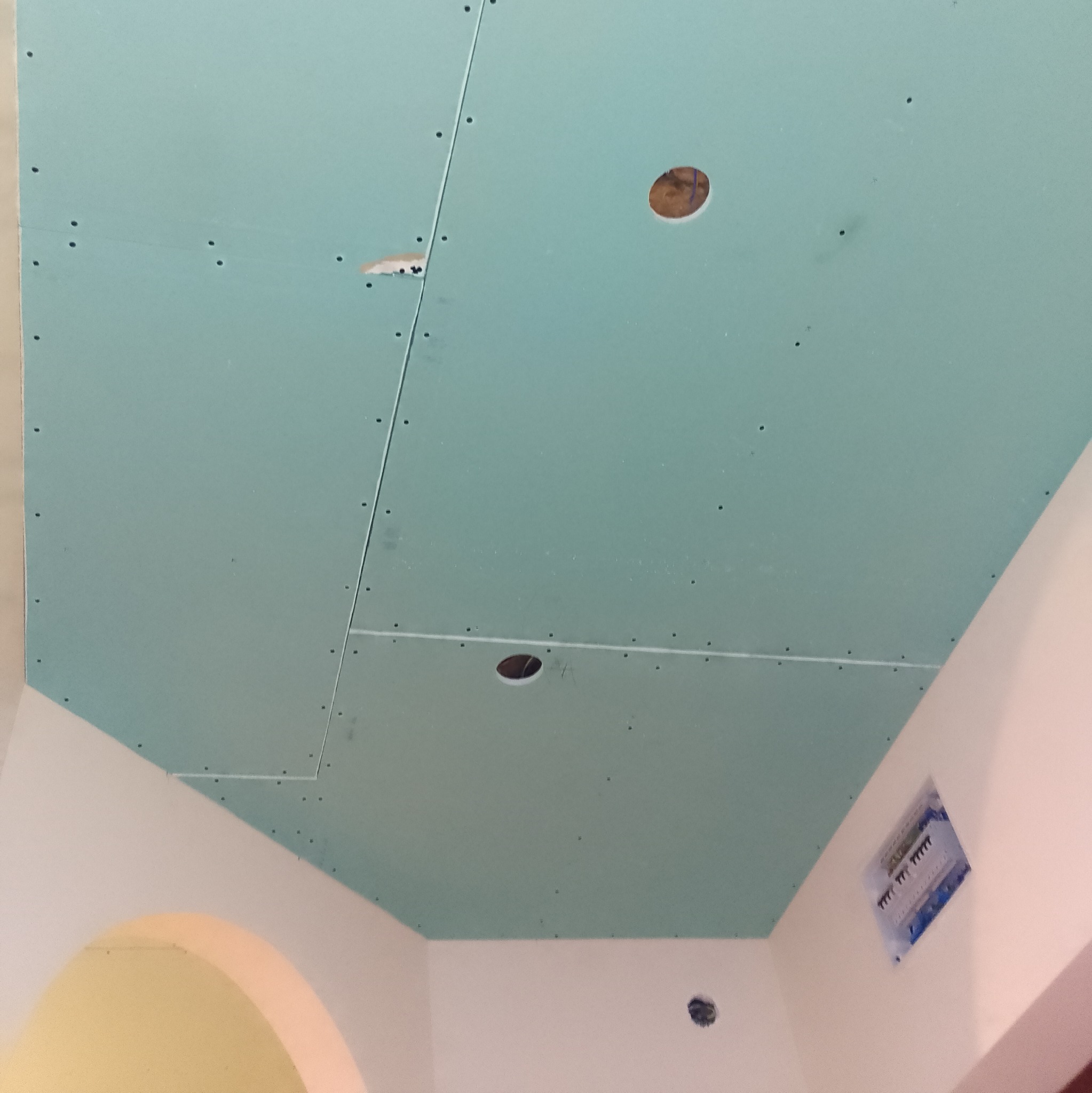 Montaż sufitu podwieszanego z płyty karton gips z wyciętymi otworami na oświetlenie punktowe, widoczne ślady szpachlowania na łączeniach płyt.