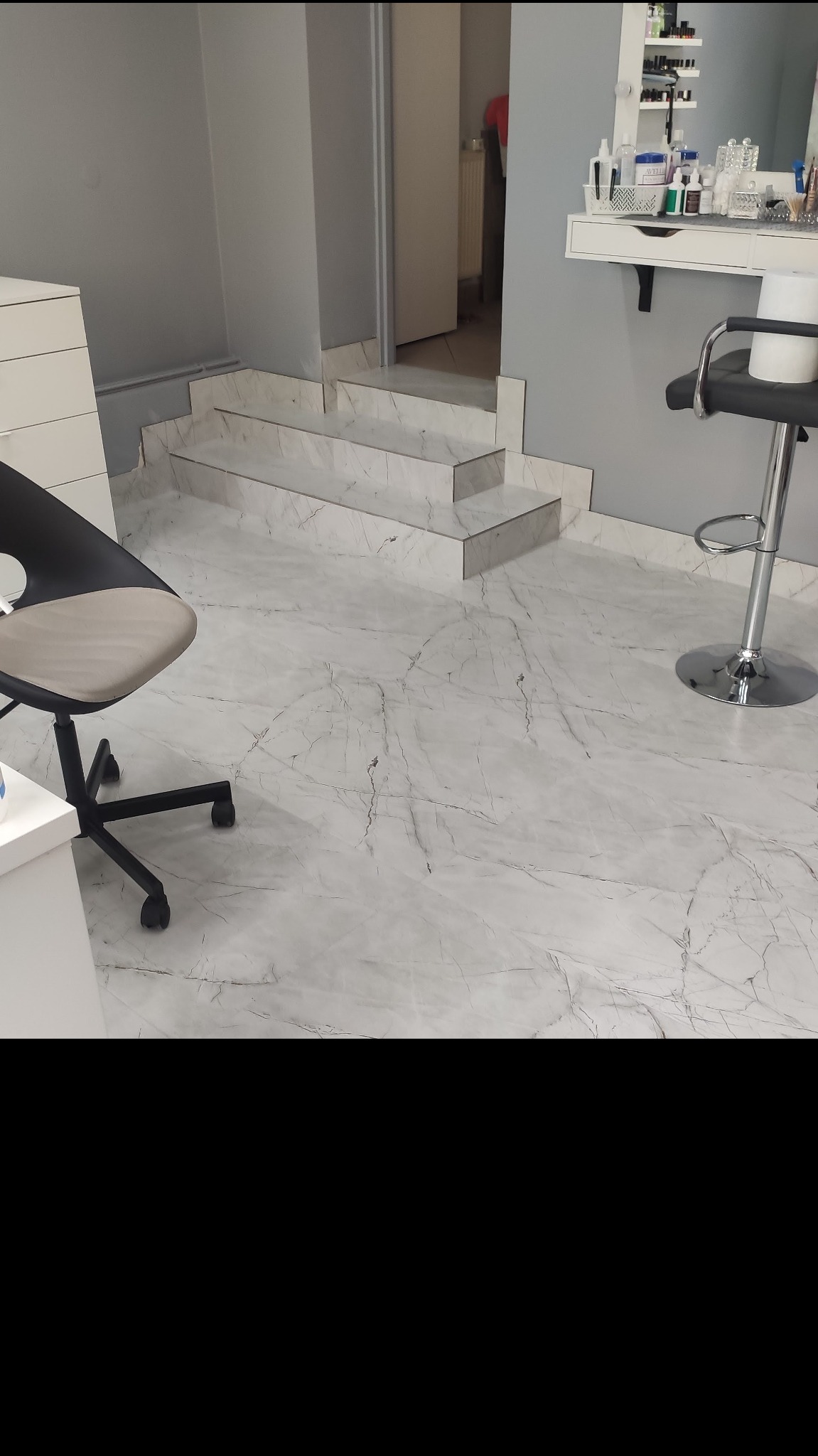 Jasnoszara marmurowa podłoga i schody w salonie kosmetycznym, widoczny fragment krzesła biurowego i stołek barowy.