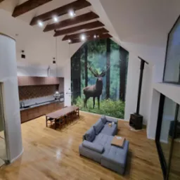 Przestronny salon z drewnianą podłogą, szarą sofą, stołem jadalnym i fototapetą z motywem jelenia w lesie, widok z góry.