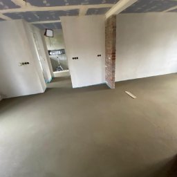 Usługi ogólnobudowlane Hubert Narloch - Wnętrze w trakcie prac wykończeniowych: wylana posadzka, ściany przygotowane pod gładzie, widoczne instalacje elektryczne. Fragment ściany z cegły.