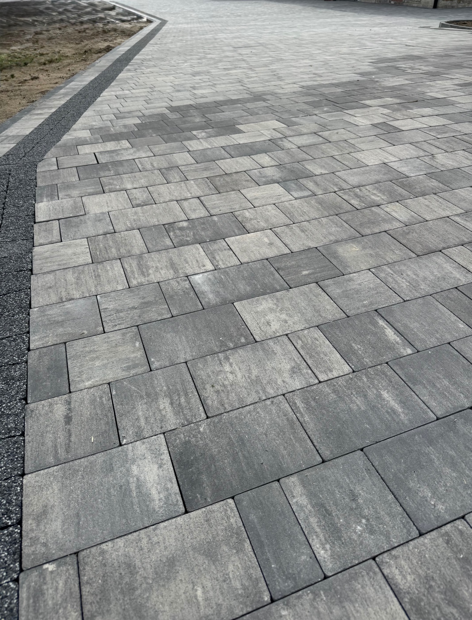 Ułożona, szara kostka brukowa o prostokątnym kształcie, z obrzeżem z drobnego kamienia. Widok z góry, ukazujący regularny wzór i estetyczne wykończenie.