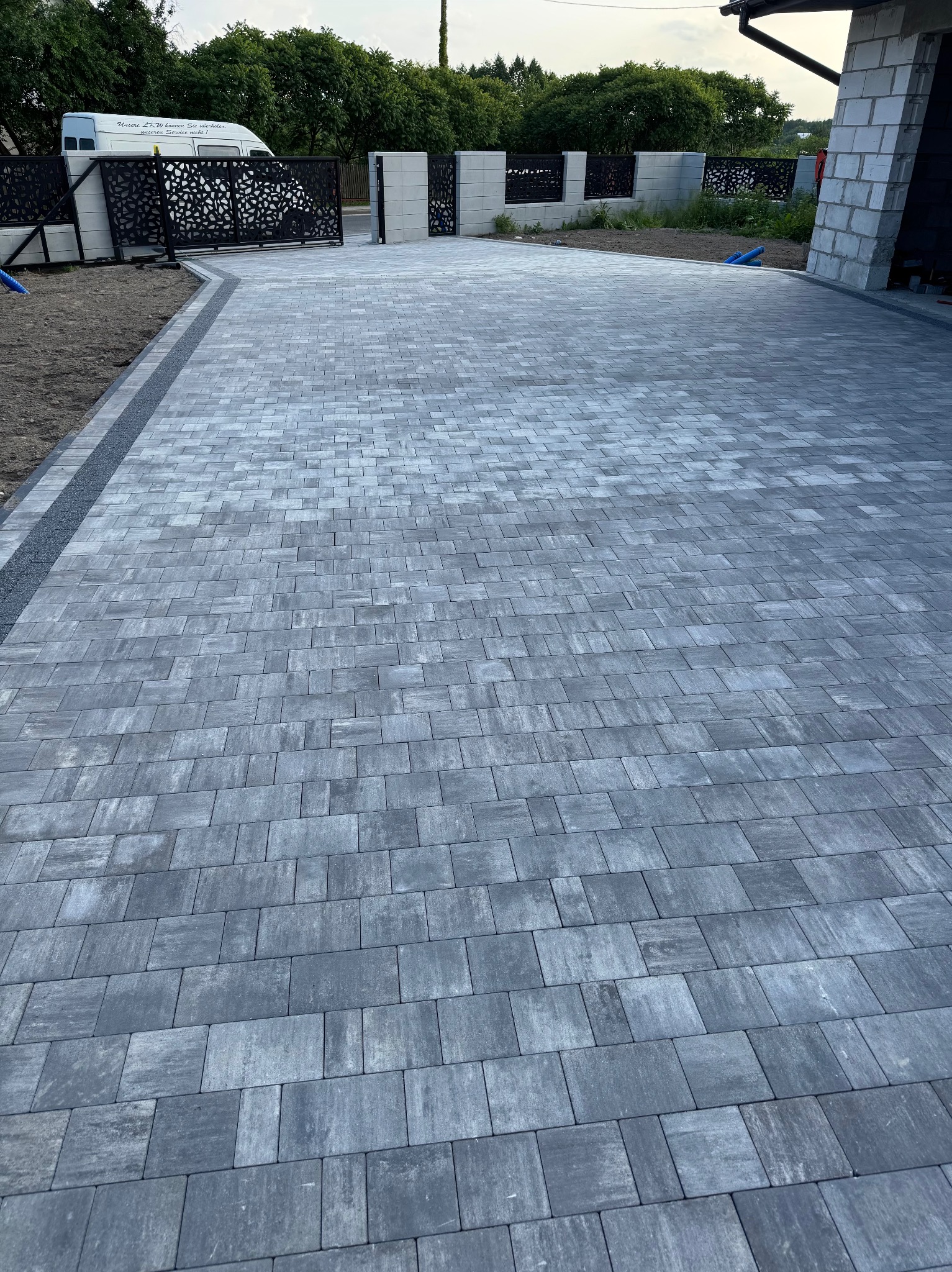 Ułożona szara kostka brukowa na podjeździe, widok z góry, z dekoracyjnym ogrodzeniem i wjazdem w tle. Nowoczesne wzornictwo.