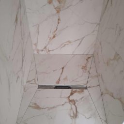 Łuk Drew Paweł Czekalinski - Wykończona kabina prysznicowa z białych płytek imitujących marmur z odpływem liniowym w podłodze.