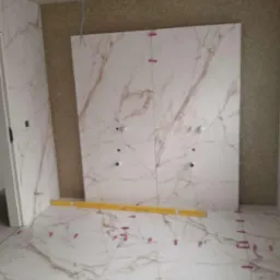 Układanie płytek imitujących marmur w łazience, widoczne poziomica i klipsy dystansowe, instalacja pod armaturę częściowo zamontowana.