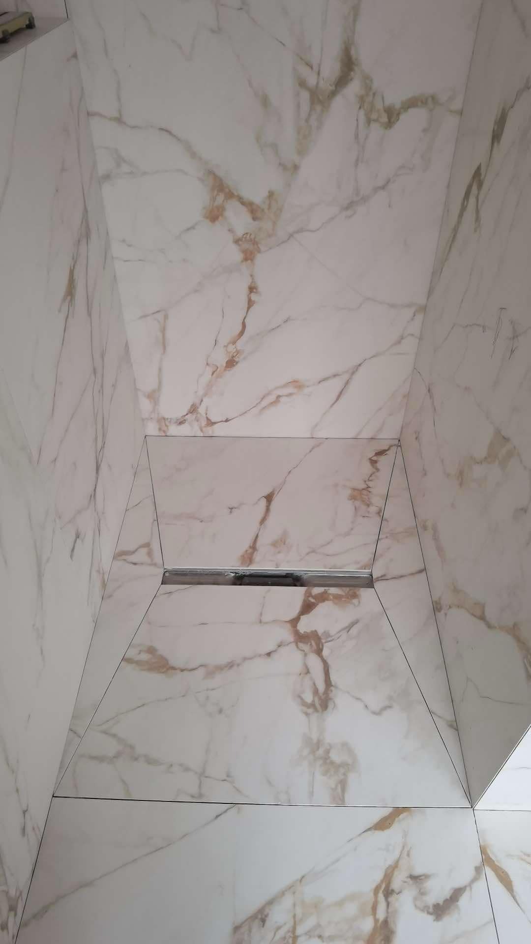 Wykończona kabina prysznicowa z białych płytek imitujących marmur z odpływem liniowym w podłodze.