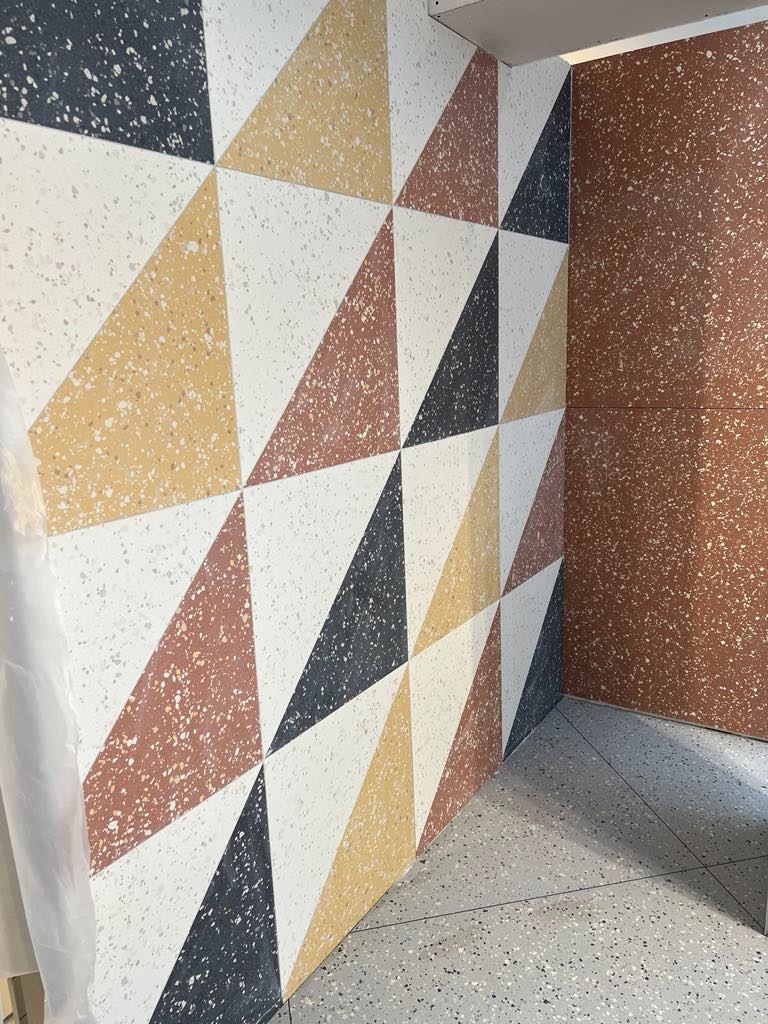 Ściana i podłoga wykończone mozaiką z trójkątnych płytek w kolorach: białym, czarnym, żółtym i brązowym, tworzących geometryczny wzór.