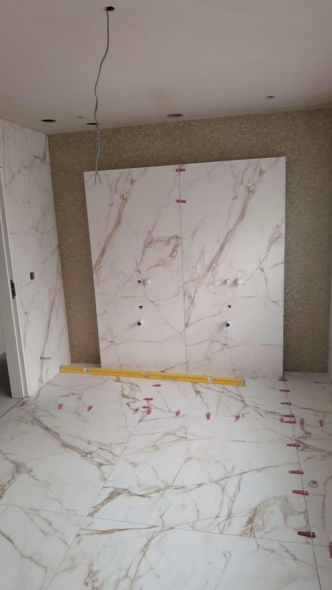 Układanie płytek imitujących marmur w łazience, widoczne poziomica i klipsy dystansowe, instalacja pod armaturę częściowo zamontowana.