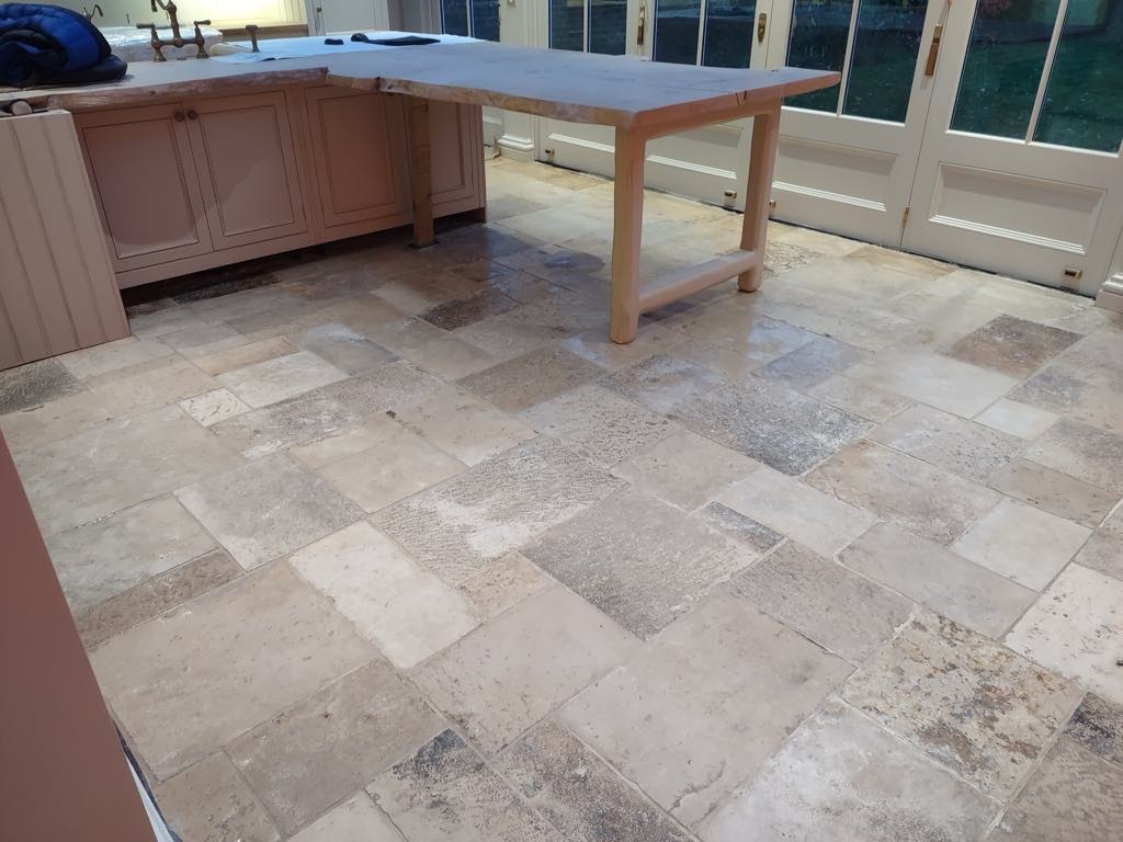 Wykończona podłoga z nieregularnych, beżowych płytek kamiennych w kuchni z wyspą i przeszklonymi drzwiami balkonowymi.