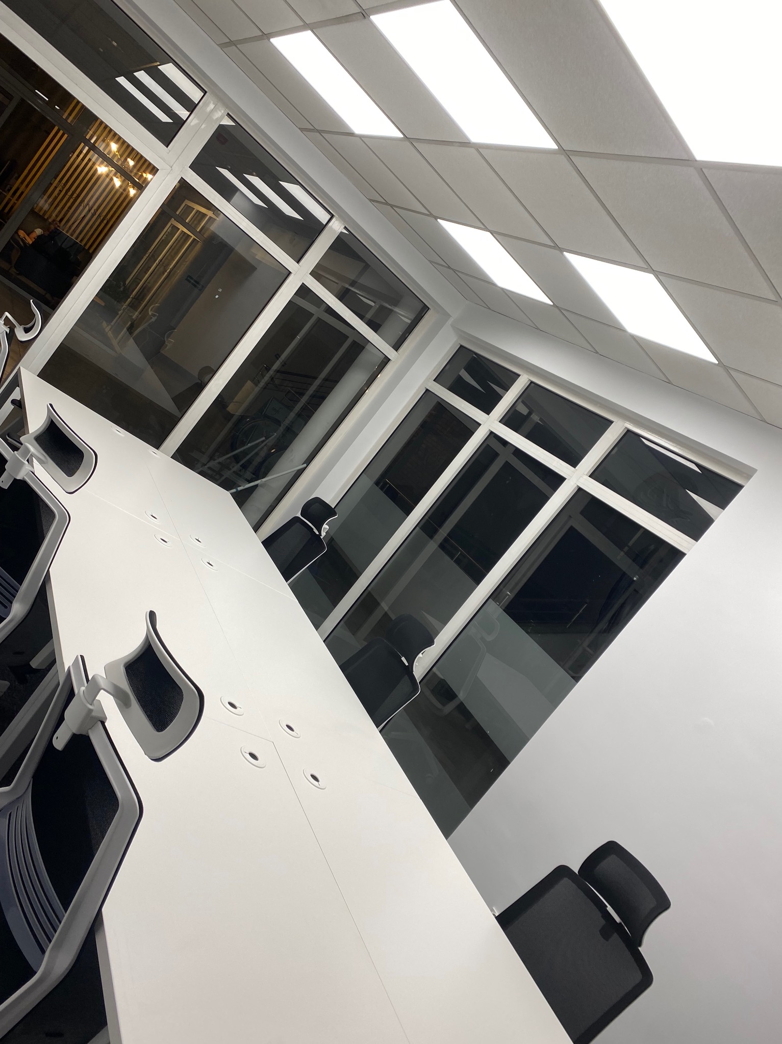 Nowoczesne biuro po remoncie: białe ściany, duże okna, designerskie krzesła i stół konferencyjny. Minimalistyczny wystrój, jasne oświetlenie.