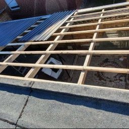 Atila dekarz - Montaż drewnianej konstrukcji dachu z widoczną częścią pokrycia z blachy trapezowej oraz pracownikiem na dachu budynku.