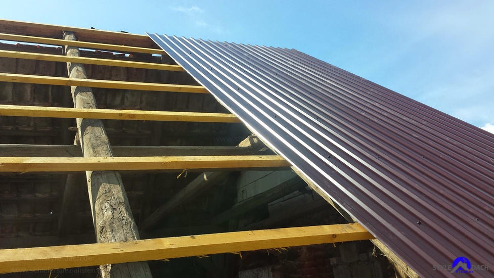 Montaż brązowej blachy profilowanej na konstrukcji drewnianej dachu, widok z dołu na niebieskie niebo.