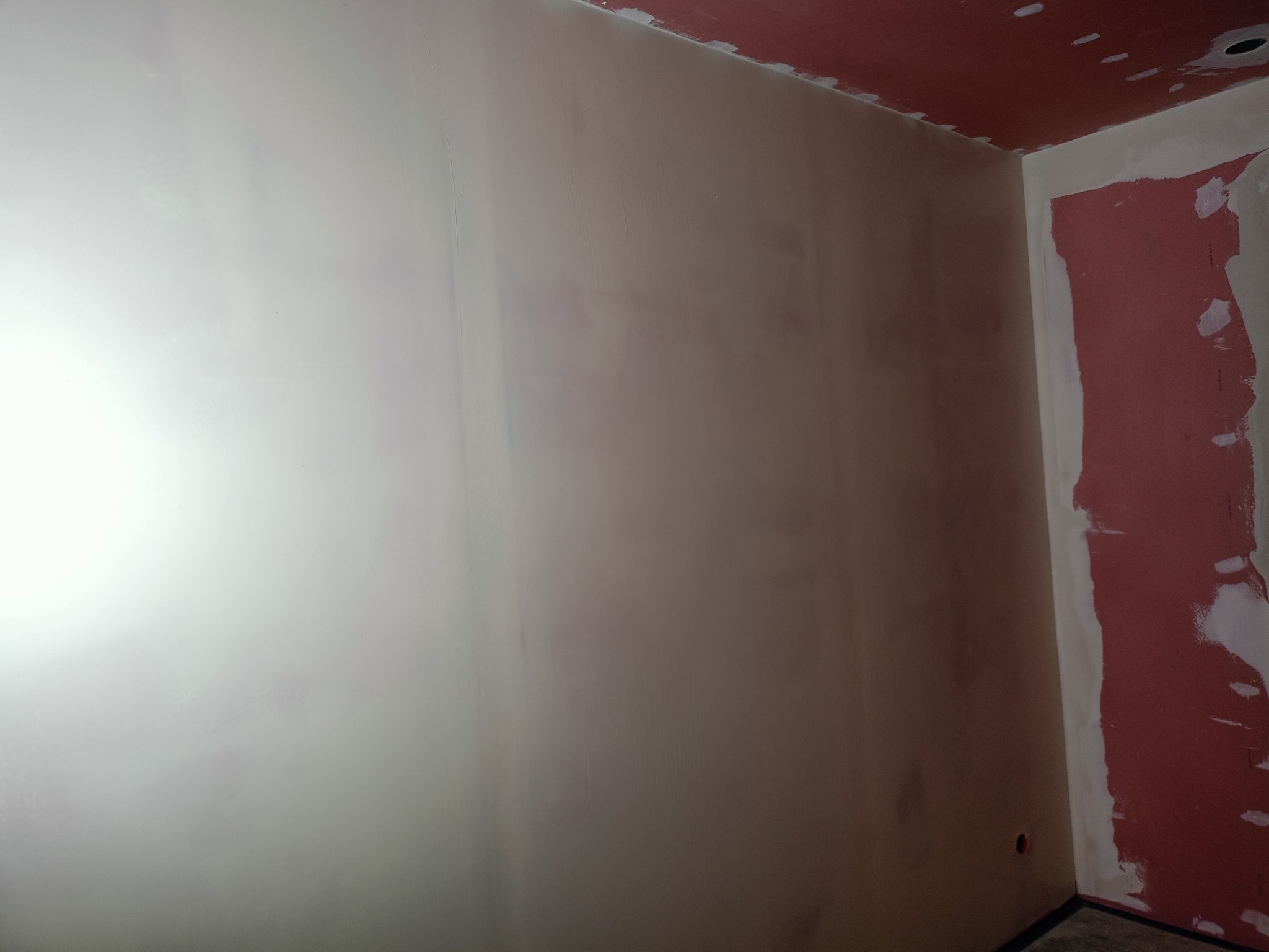 Ściana po szpachlowaniu w Bydgoszczy, przygotowana do malowania. Widoczne ślady po łatach gipsowych i nierówności. Sufit i fragment ściany w kolorze czerwonym.