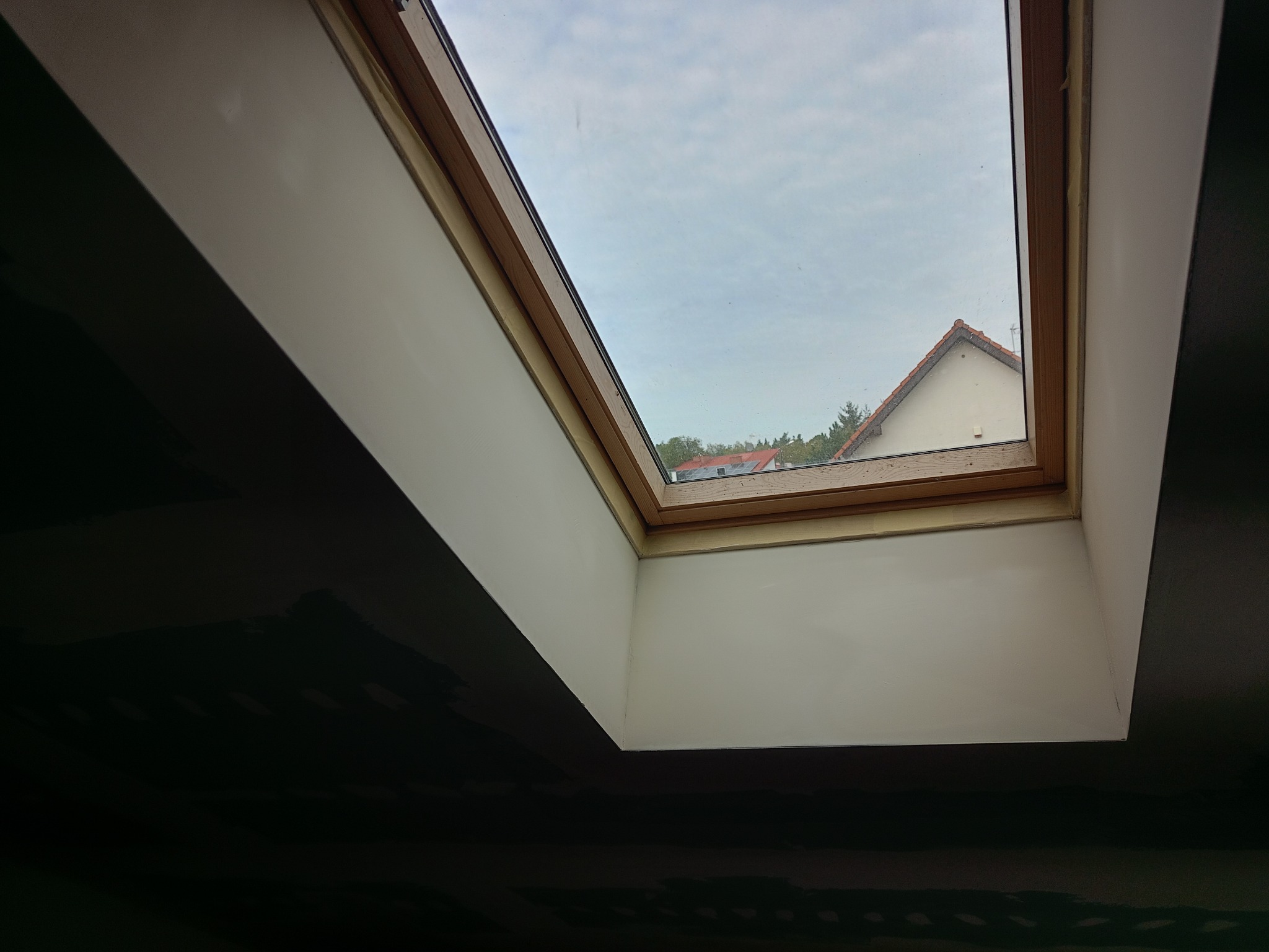 Wnętrze po malowaniu z oknem dachowym, widok na niebo i dach budynku. Ściany w kontrastowych kolorach: biały przy oknie i ciemny poniżej.