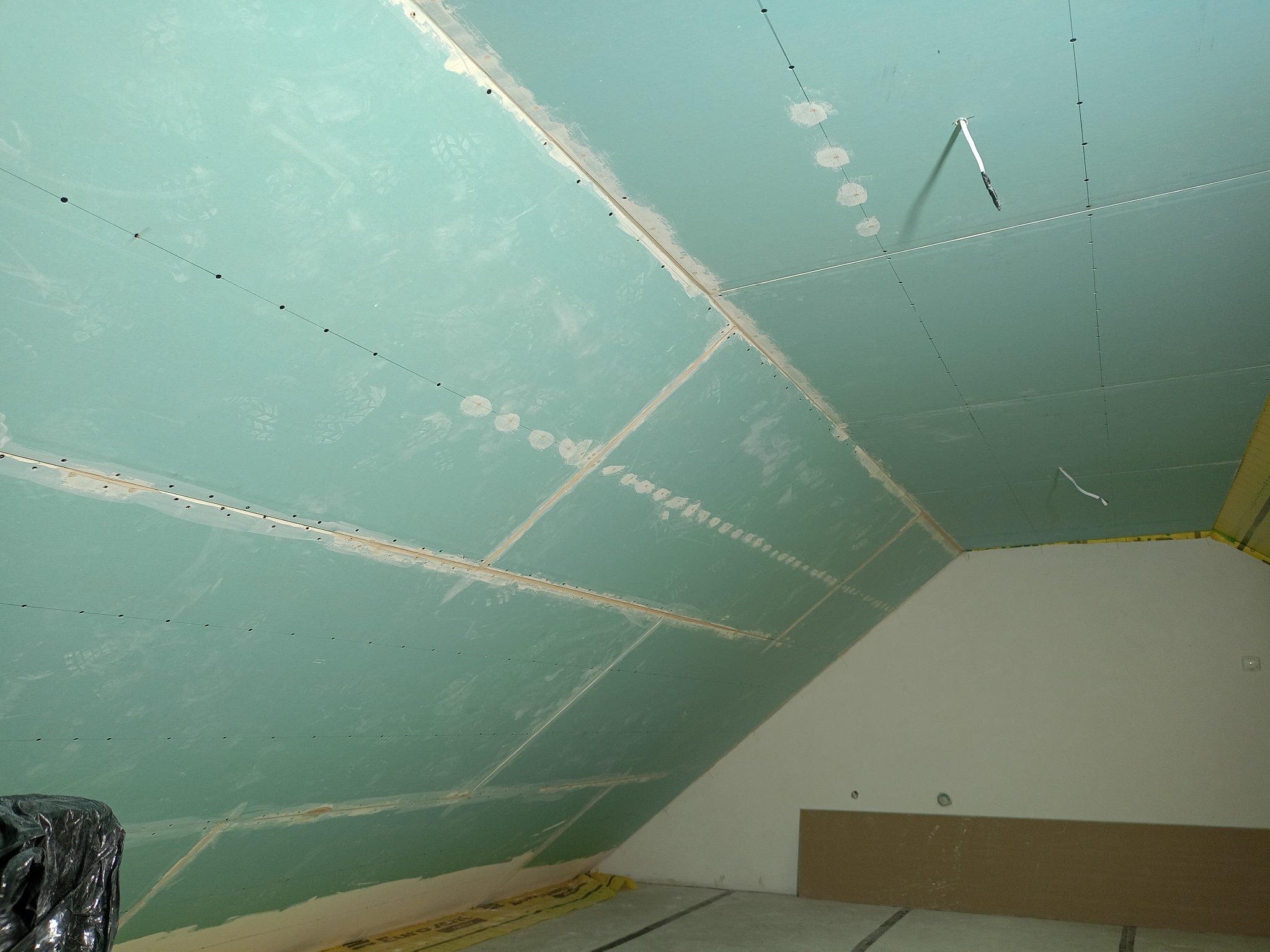 Skośny sufit na poddaszu wykończony zielonymi płytami kartonowo-gipsowymi, widoczne łączenia płyt i ślady szpachlowania, przygotowanie do dalszych prac wykończeniowych.
