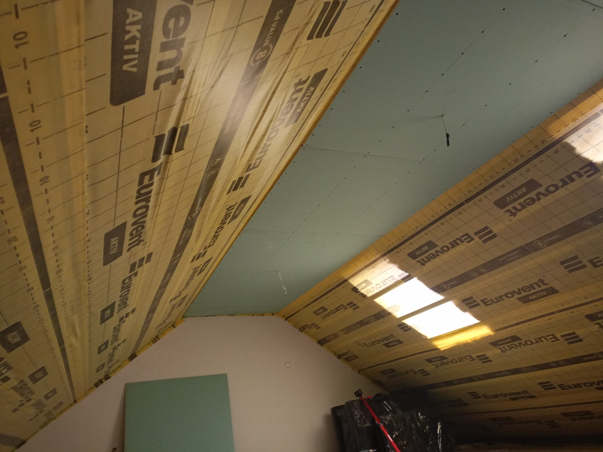 Poddasze w trakcie wykańczania: widoczna membrana Eurovent i płyty kartonowo-gipsowe na skośnym suficie. W tle fragment ściany i narzędzia.