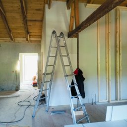 constructionmonter@gmail.com - Wnętrze w trakcie remontu: ściany z płyt karton-gips, drewniany strop, metalowa drabina rozstawiona, widoczne kable na podłodze i elementy konstrukcyjne ściany działowej.
