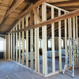 constructionmonter@gmail.com - Konstrukcja ścian działowych z drewnianych belek na poddaszu z drewnianą boazerią, widoczne rusztowania i materiały budowlane w tle.